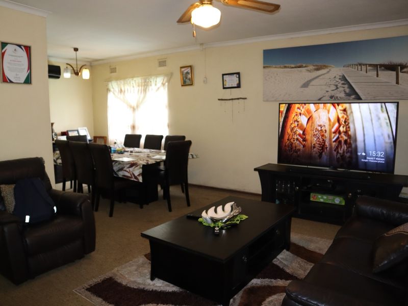Spacious open-plan living and dining area featuring carpeted flooring, a ceiling fan, and neutral wall finishes.