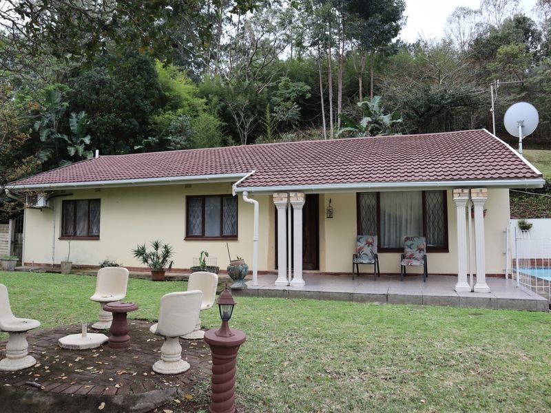 Rear view of a single-story home featuring a covered patio, tiled roof, and a spacious garden area with a paved seating section.