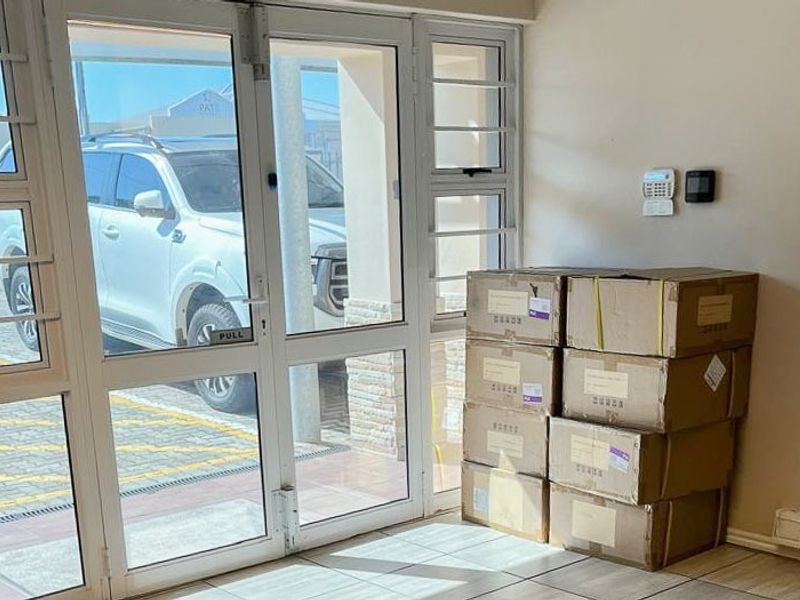 A bright commercial entry area featuring tiled flooring, an aluminium-framed glass door with security bars, and an installed alarm system.