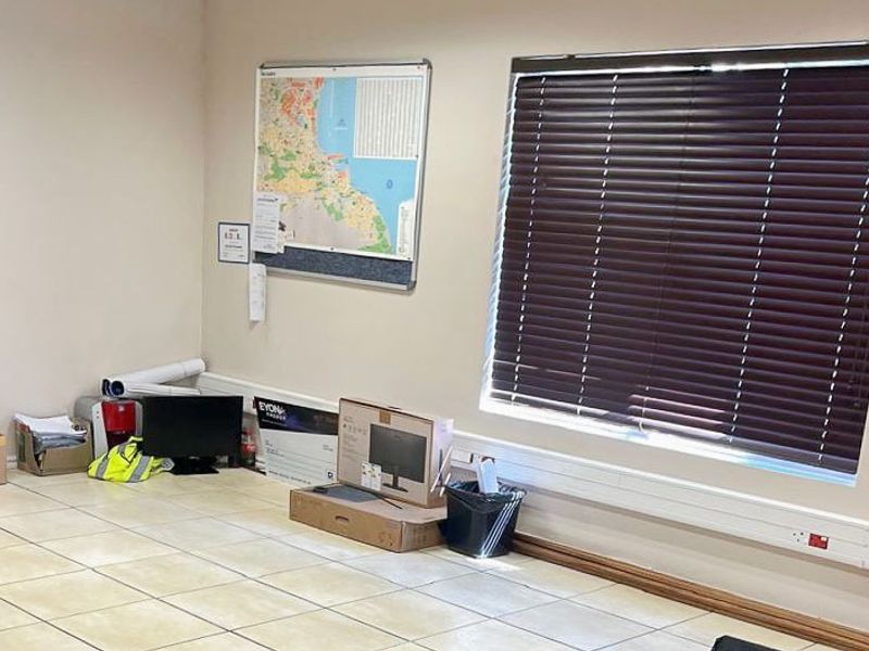 A functional office space featuring tiled flooring, surface-mounted electrical trunking, and window blinds, providing a clean and practical commercial work environment.