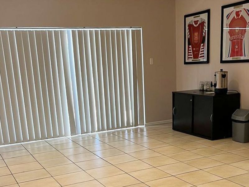 A functional living area featuring neutral tiled flooring and large vertical blinds, providing a clean and versatile space for various commercial uses.