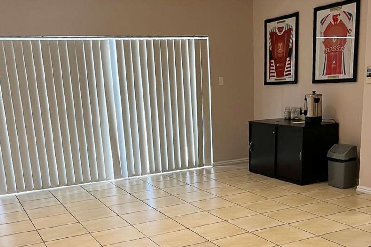 A functional living area featuring neutral tiled flooring and large vertical blinds, providing a clean and versatile space for various commercial uses.