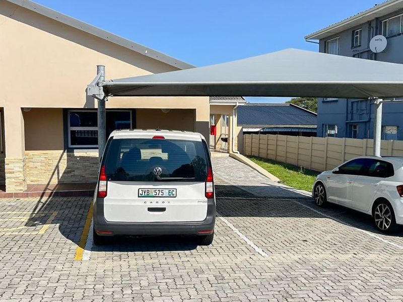 Commercial property exterior featuring a paved parking area with a shade cloth carport structure and stone cladding accents on the building facade.