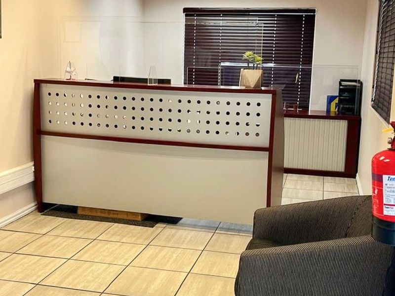 A professional commercial reception area featuring a built-in reception desk, tiled flooring, and essential fire safety equipment.