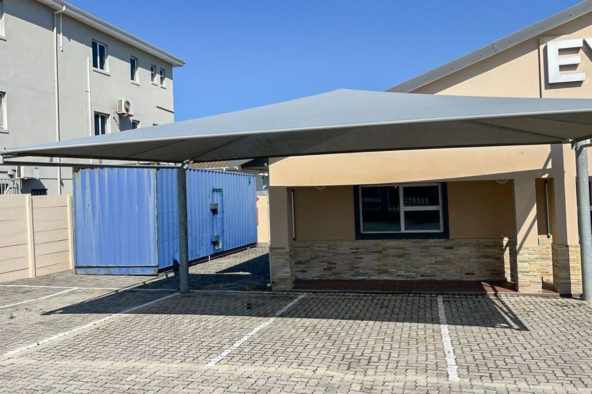 Commercial exterior view featuring a paved parking area with a shade port, stone-clad facade details, and a secure boundary wall.