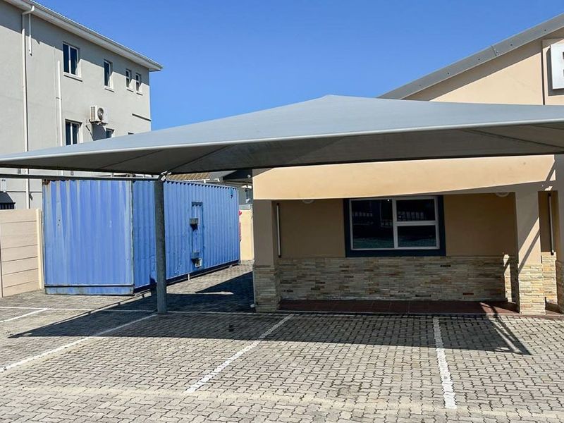 Commercial exterior view featuring a paved parking area with a shade port, stone-clad facade details, and a secure boundary wall.