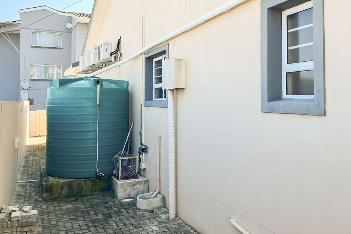 Rear exterior area featuring a water storage tank, external air conditioning units, and paved access path along the building side.