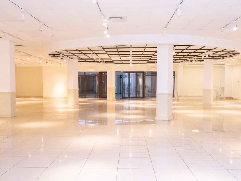 A spacious, open-plan commercial interior featuring polished tile flooring, structural columns, and modern recessed track lighting, suitable for retail or office use.