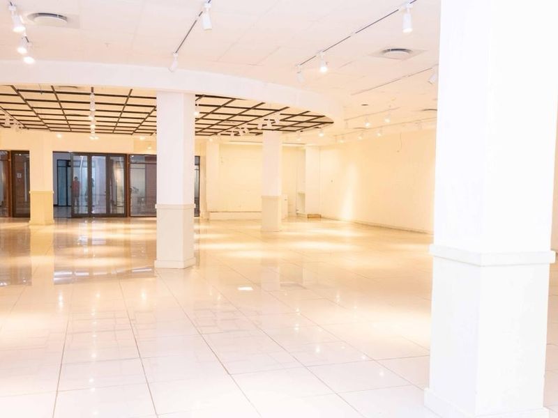 A spacious, open-plan commercial interior featuring polished tiled flooring, structural columns, and a combination of recessed and track lighting throughout the area.