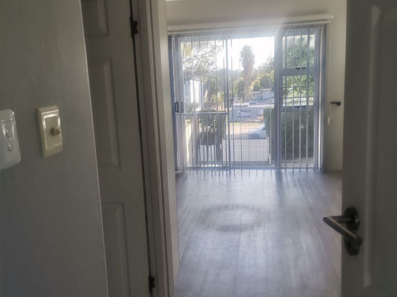 An empty living area featuring light-toned laminate flooring, recessed ceiling lighting, and a sliding glass door with vertical blinds leading to an outdoor space.