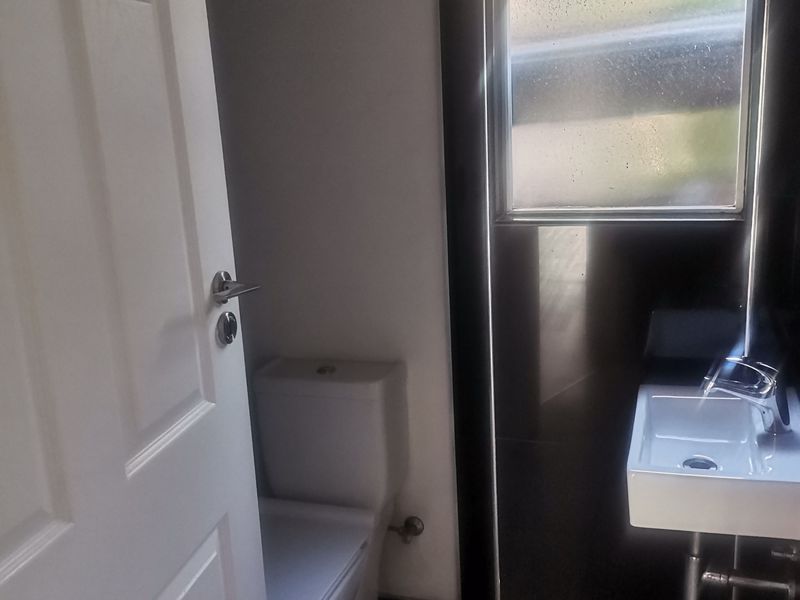 A compact, modern bathroom featuring a wall-mounted basin, a standard toilet, and tiled flooring with natural light from a window.