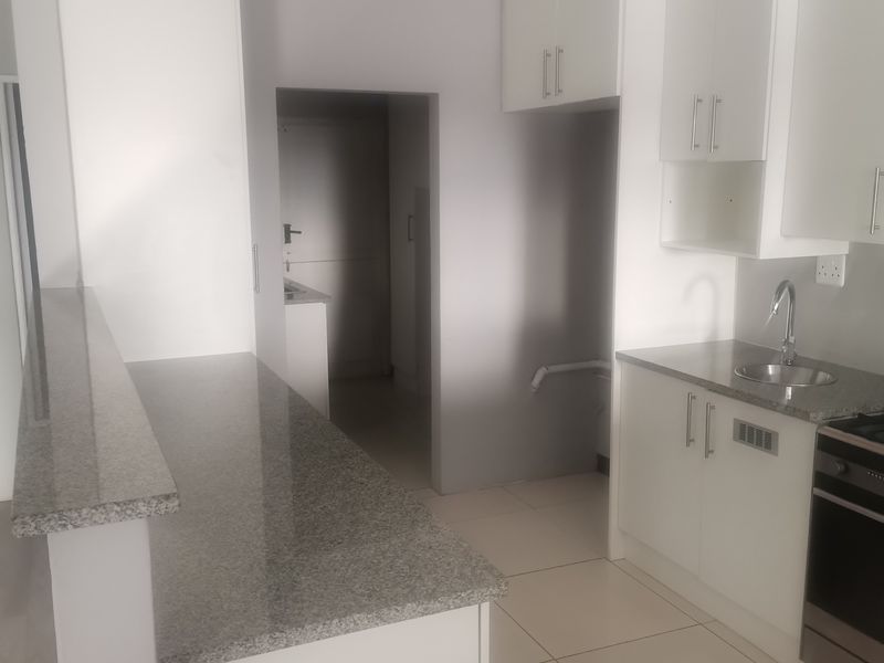 A clean, modern kitchen featuring white cabinetry, granite countertops, tiled flooring, and a stainless steel sink, presenting a bright and functional workspace.