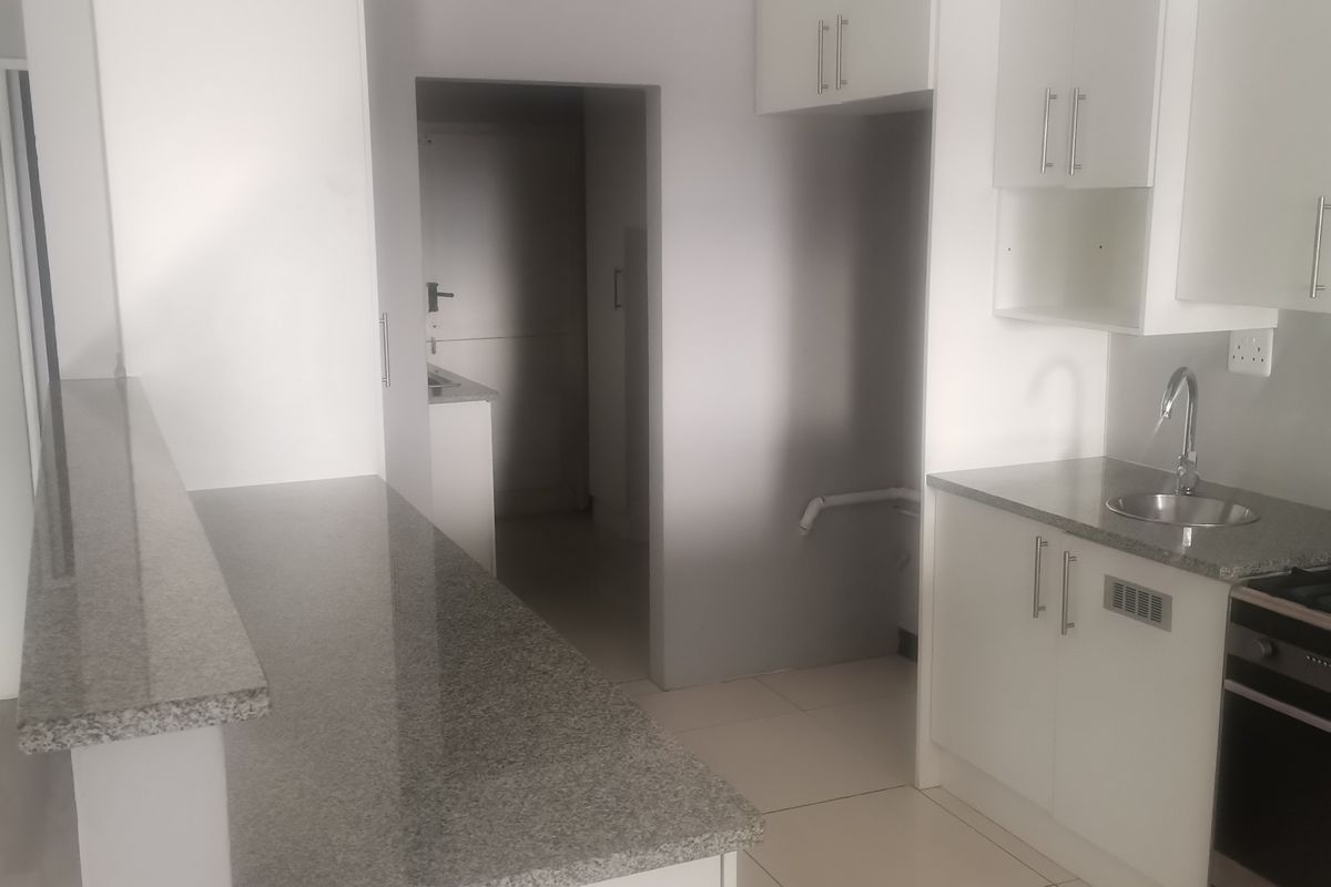 A clean, modern kitchen featuring white cabinetry, granite countertops, tiled flooring, and a stainless steel sink, presenting a bright and functional workspace.
