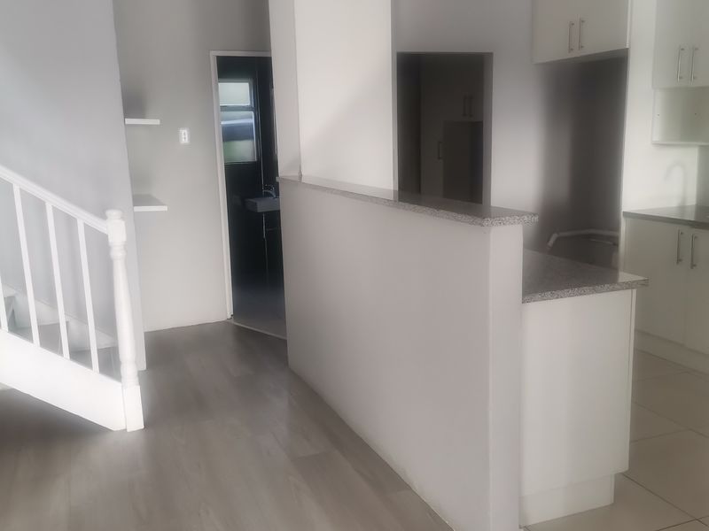An open-plan living area featuring a staircase, neutral laminate and tiled flooring, and a modern kitchen with white cabinetry and granite countertops.