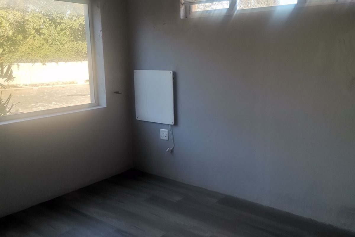 An empty bedroom featuring laminate flooring, a ceiling fan, and a wall-mounted heater, with natural light provided by two windows.