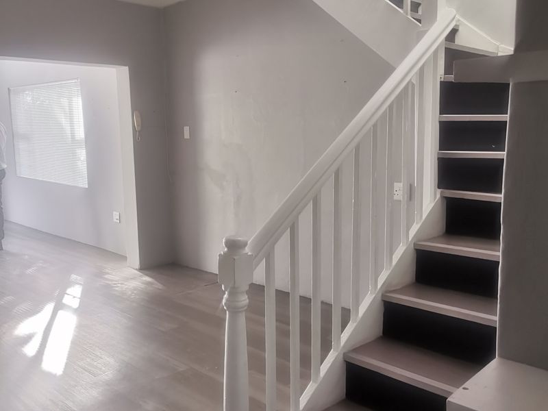An empty entrance area featuring a staircase with a white balustrade and light-toned laminate flooring, leading into an open-plan living space.