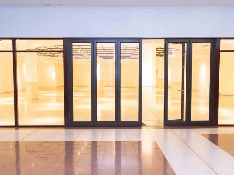 A spacious, vacant retail unit featuring a large glass storefront, tiled flooring, and recessed ceiling lighting, offering a clean and open layout.
