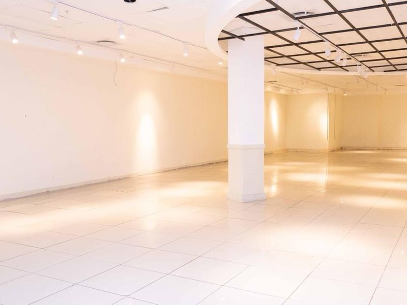 A spacious, vacant retail unit featuring polished tiled flooring, structural columns, and a combination of recessed track and grid ceiling lighting.