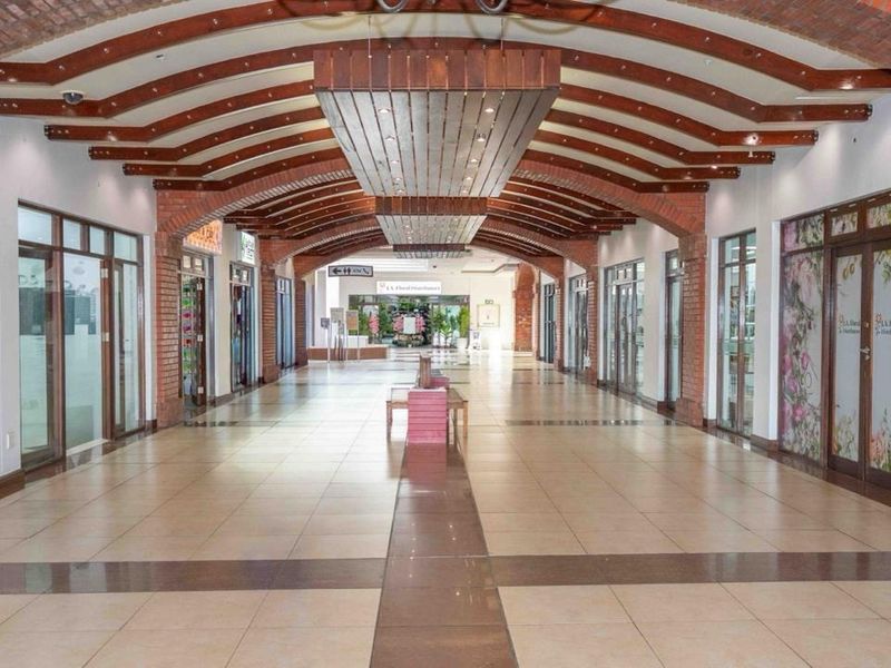 A spacious retail corridor featuring decorative exposed brick arches, timber ceiling beams, and polished tiled flooring with multiple glass-fronted shop units.