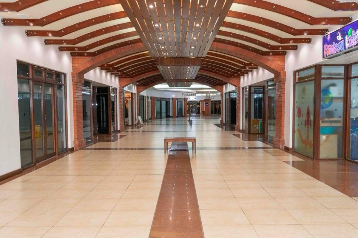A spacious retail mall corridor featuring decorative timber ceiling beams, exposed brick archways, and polished tiled flooring with multiple glass-fronted shop units.