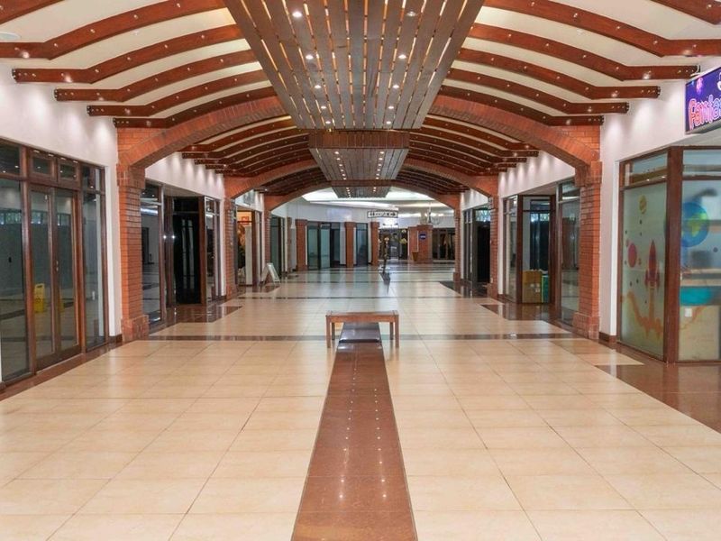 A spacious retail mall corridor featuring decorative timber ceiling beams, exposed brick archways, and polished tiled flooring with multiple glass-fronted shop units.