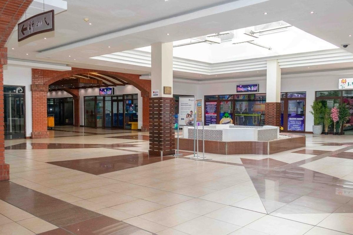 Spacious retail mall interior featuring a central skylight, decorative brick archways, polished tiled flooring, and a central fountain feature.
