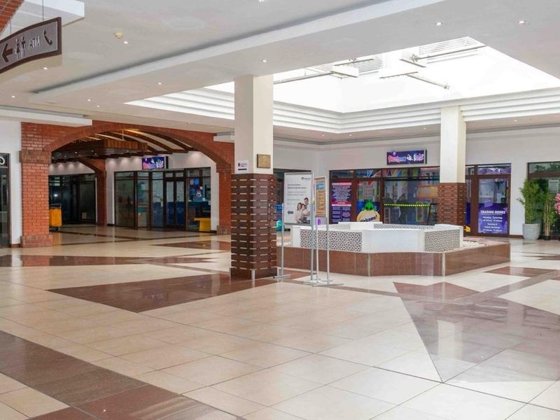 Spacious retail mall interior featuring a central skylight, decorative brick archways, polished tiled flooring, and a central fountain feature.