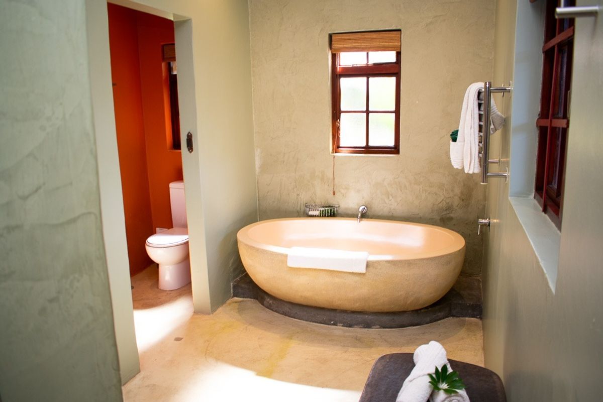 A bathroom featuring a large freestanding bathtub, a separate toilet area, and a heated towel rail with a rustic, textured wall finish.