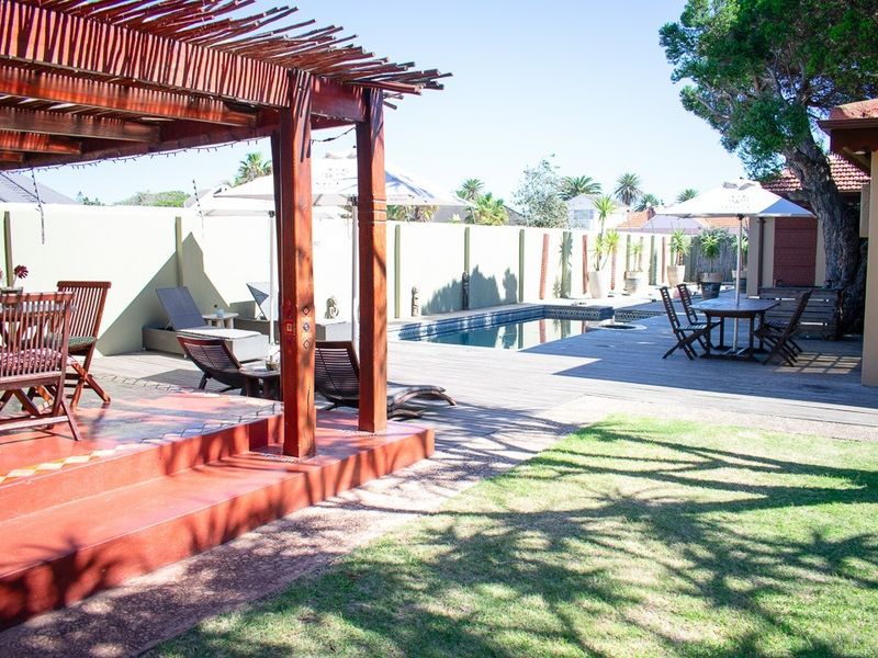 Outdoor entertainment area featuring a swimming pool, wooden decking, and a covered timber pergola, set within a private garden space.