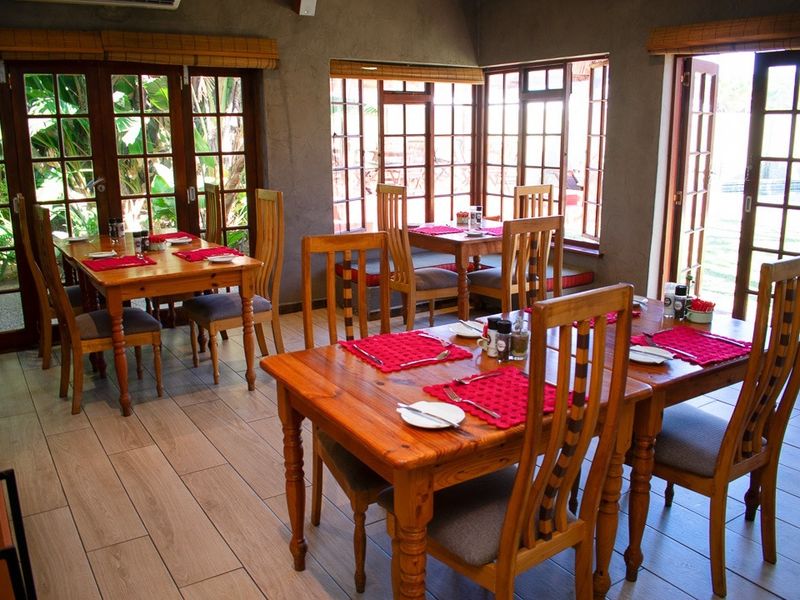 A spacious dining area featuring tiled flooring, multiple wooden-framed french doors providing garden access, and large windows allowing for ample natural light.