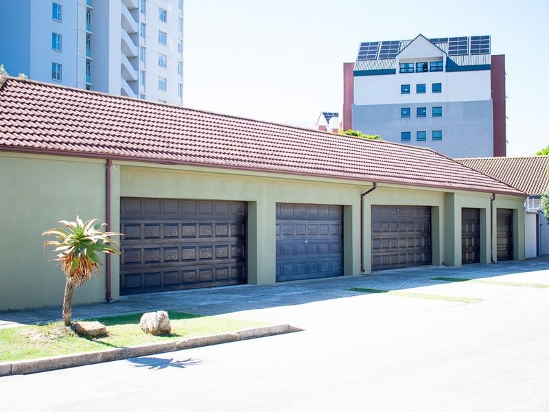 A row of multiple secure garage bays with dark panelled doors and a tiled roof, situated in a paved driveway area.