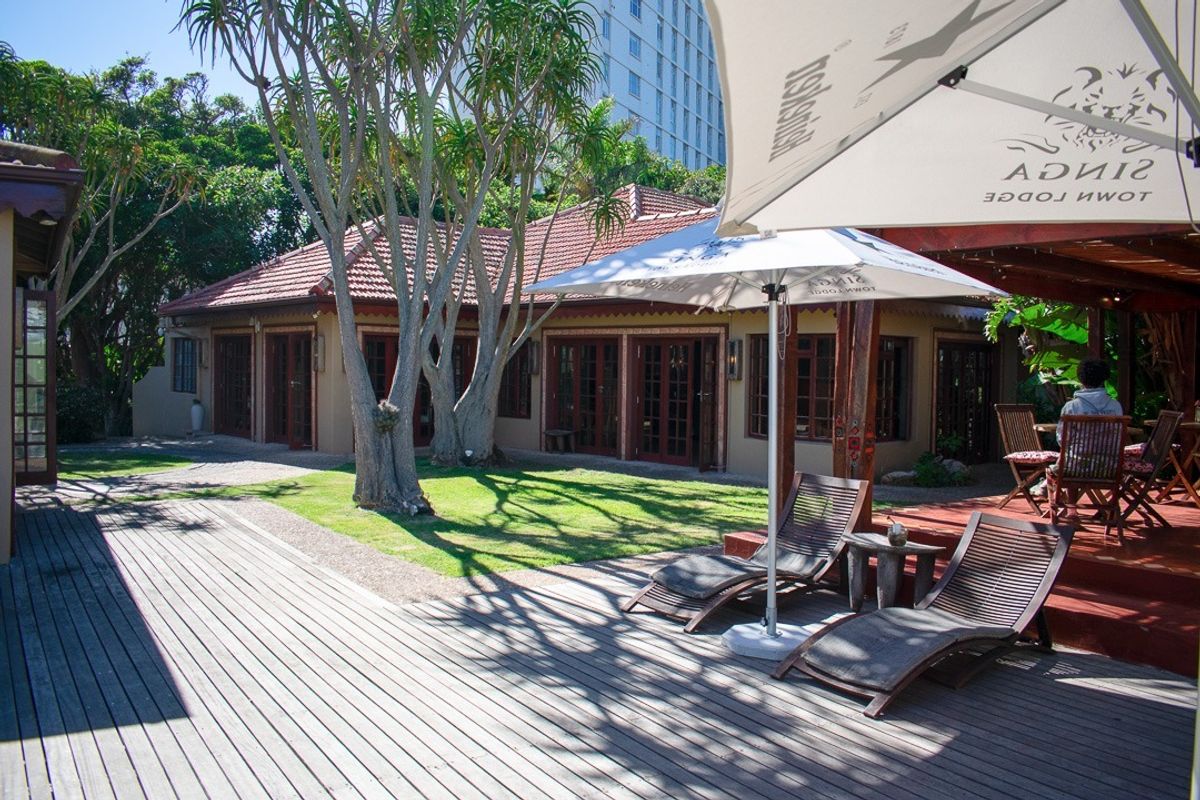 A well-maintained rear exterior view featuring a wooden deck, landscaped garden, and covered patio area with access to the main building via french doors.