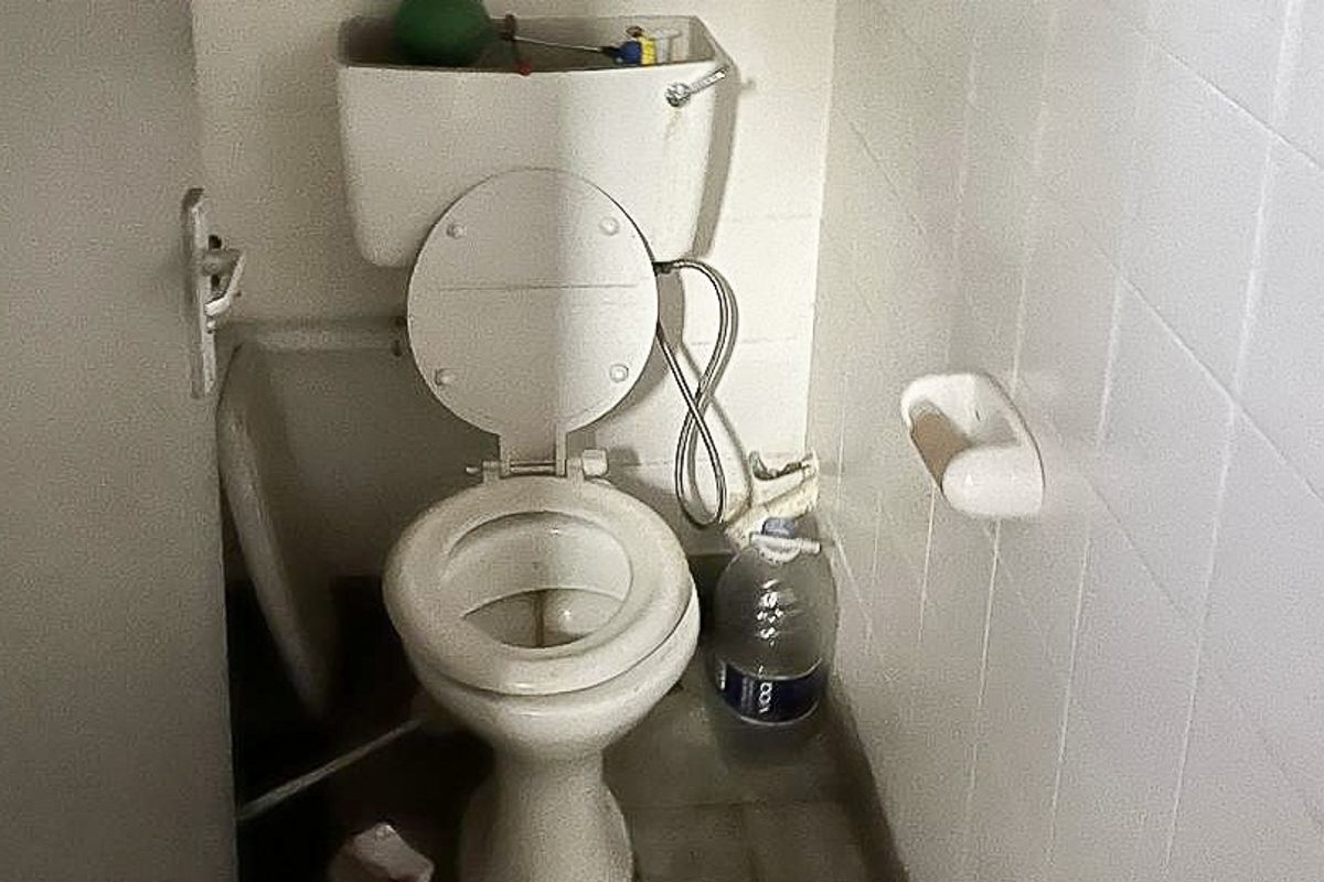 A small, dated bathroom featuring a standard toilet and white ceramic wall tiling, currently in need of maintenance and cosmetic updates.