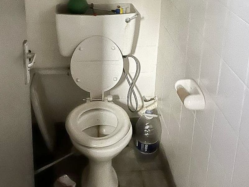A small, dated bathroom featuring a standard toilet and white ceramic wall tiling, currently in need of maintenance and cosmetic updates.