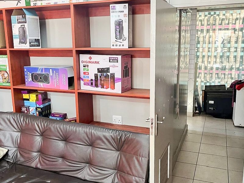 A retail utility or storage area featuring built-in wooden shelving units, tiled flooring, and direct access to an adjacent service space.