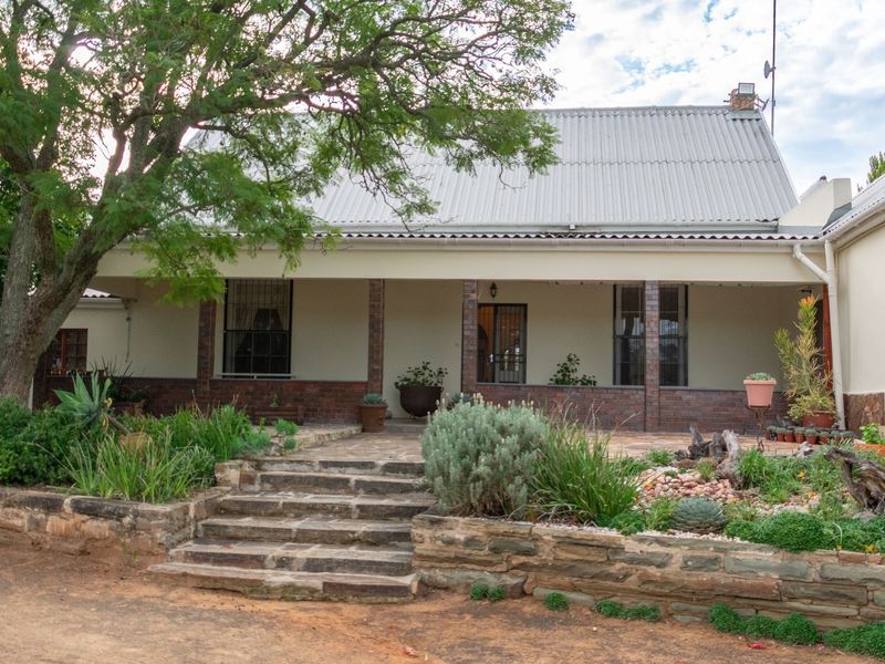 A charming farmhouse exterior featuring a covered veranda, stone steps, and a landscaped garden with a stone retaining wall.