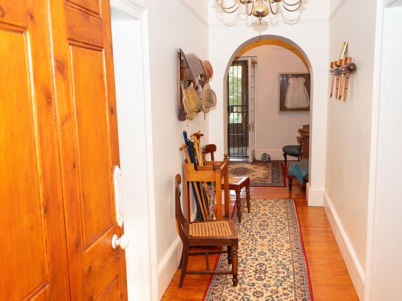 A bright hallway featuring polished hardwood flooring, a classic architectural archway, and traditional light fixtures, leading towards an exterior entrance.