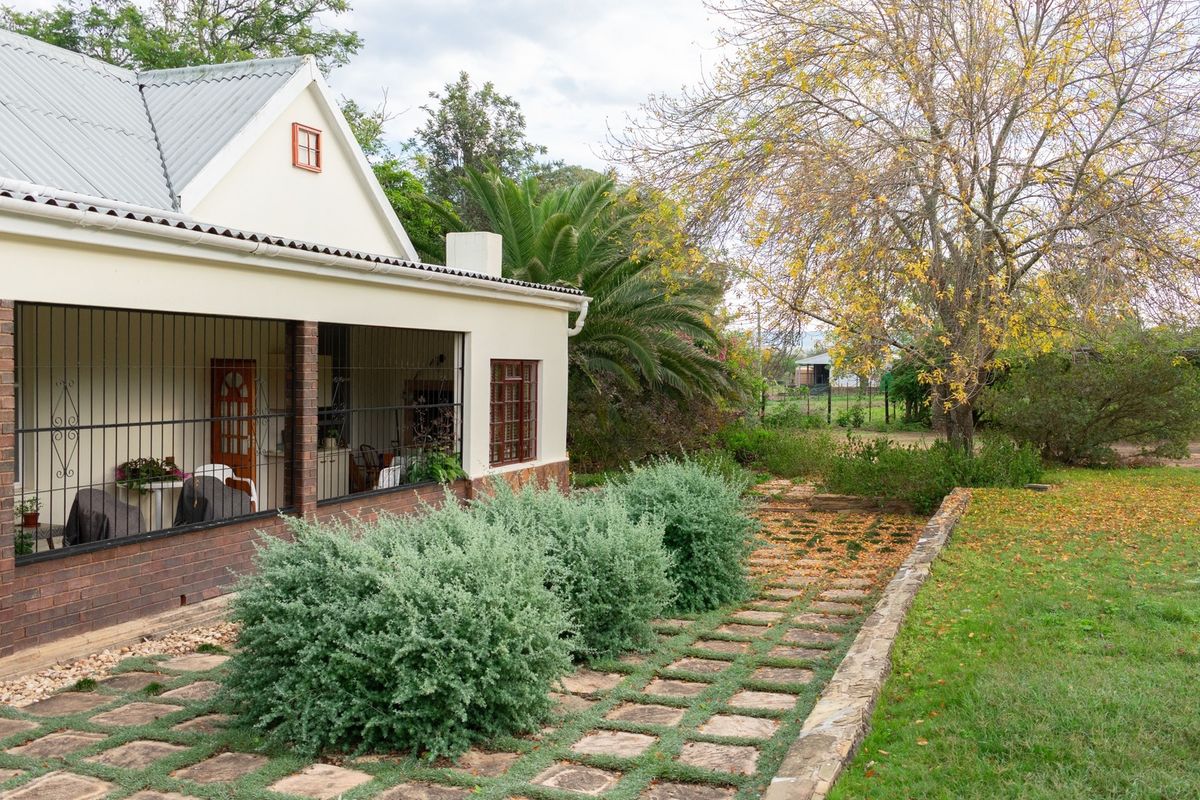 A view of the rear exterior featuring a covered patio with brick accents, security bars, and a stone-paved walkway leading into the garden.