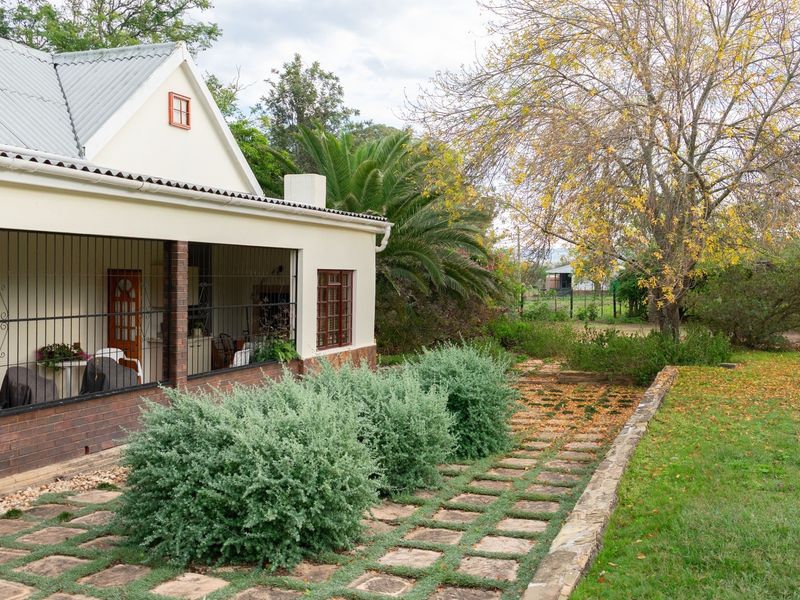 A view of the rear exterior featuring a covered patio with brick accents, security bars, and a stone-paved walkway leading into the garden.