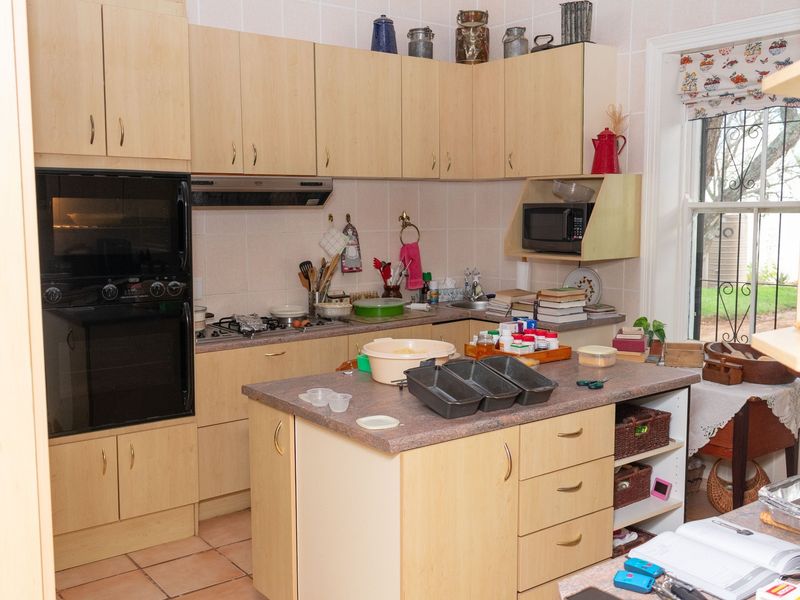A functional kitchen featuring light wood cabinetry, a central island, built-in oven, gas hob, and tiled flooring with a window overlooking the garden.