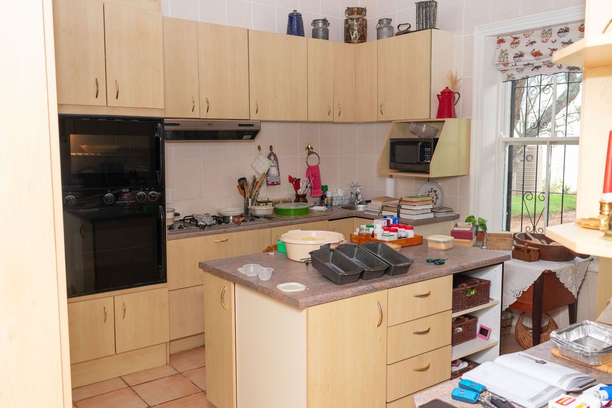 A functional kitchen featuring light wood cabinetry, a central island, built-in oven, gas hob, and tiled flooring with a window overlooking the garden.