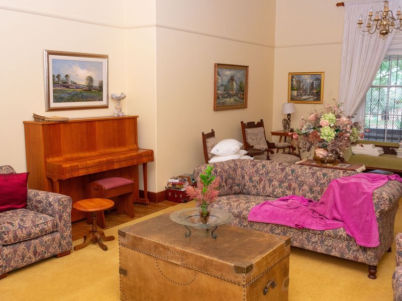A spacious living room featuring high ceilings, a classic chandelier, and a large sash window with traditional drapery.