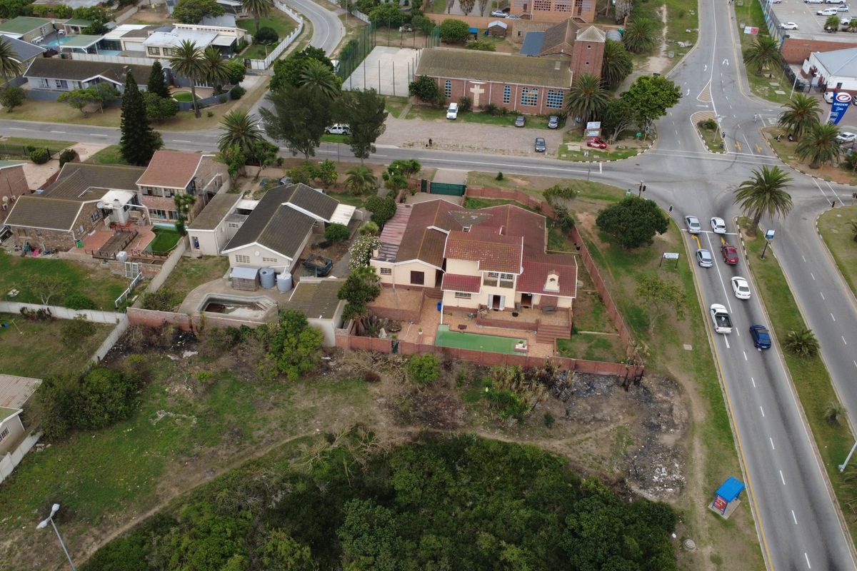 Aerial view of a residential property featuring a swimming pool, paved patio area, and surrounding garden space situated near a main road intersection.