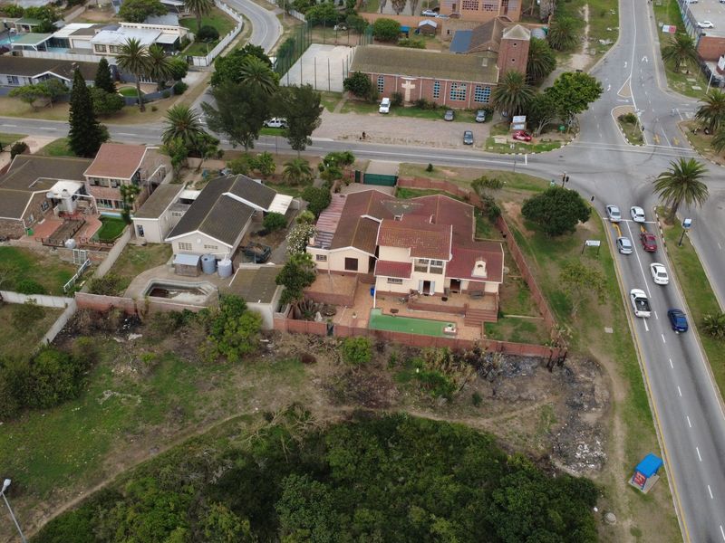 Aerial view of a residential property featuring a swimming pool, paved patio area, and surrounding garden space situated near a main road intersection.