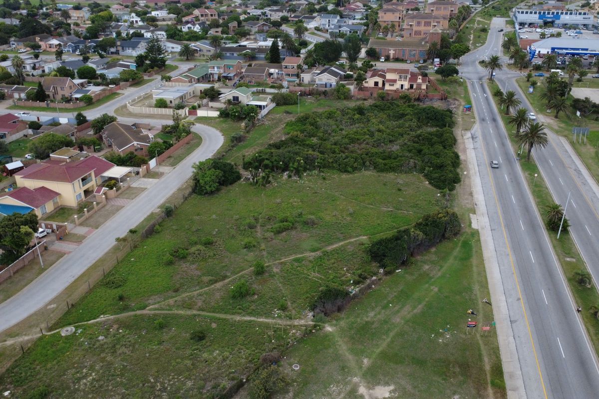 Aerial view of a vacant commercial land plot situated in a developed residential and commercial area with main road access.
