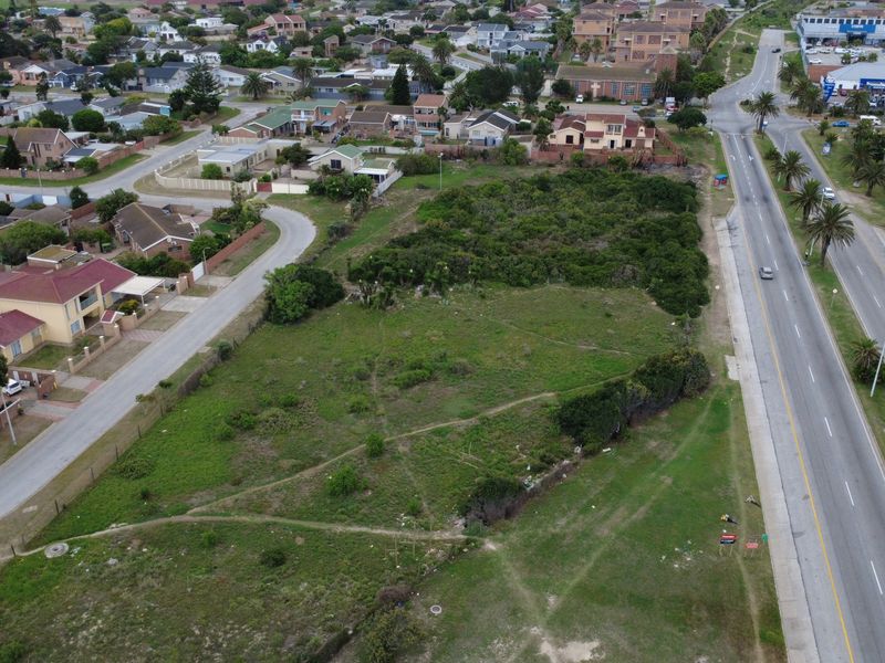 Aerial view of a vacant commercial land plot situated in a developed residential and commercial area with main road access.