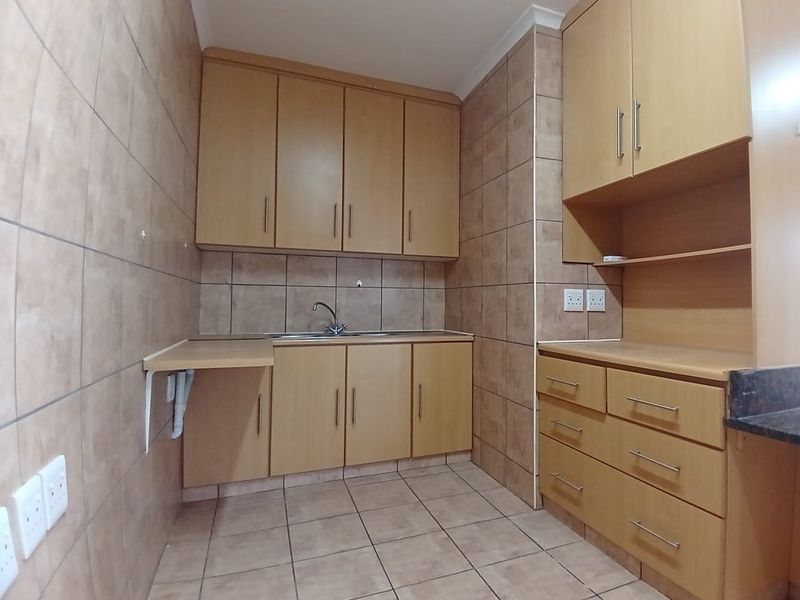 A functional kitchen area featuring light wood-tone cabinetry, tiled walls and flooring, and a built-in sink with ample storage space.