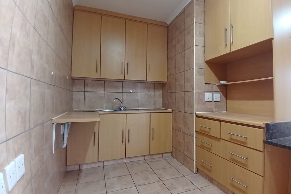A functional kitchen area featuring light wood-tone cabinetry, tiled walls and flooring, and a built-in sink with ample storage space.