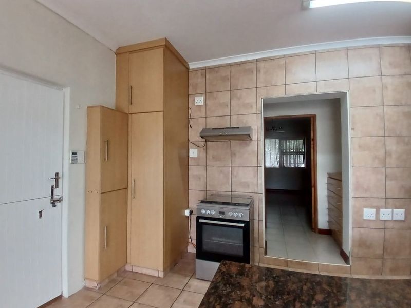 Functional kitchen featuring built-in cabinetry, granite countertops, a tiled splashback, and a freestanding stove, with direct access to an adjacent room.