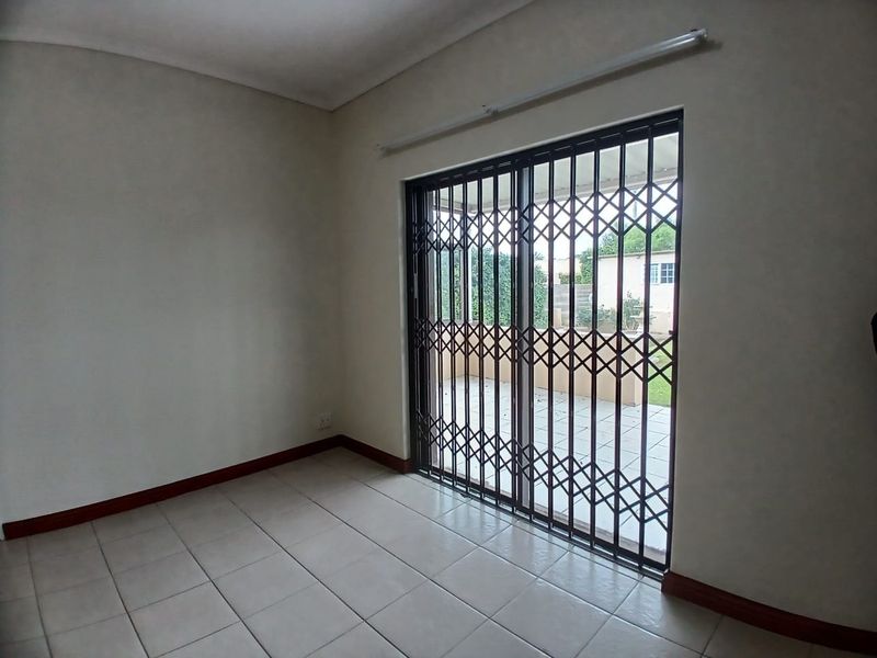 An empty living room featuring tiled flooring and a sliding glass door with a security gate, providing direct access to the outdoor patio area.